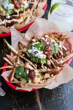 two red bowls filled with fries covered in toppings and garnished with sour cream