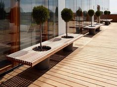 a wooden bench sitting on top of a hard wood floor next to tall windows and trees