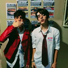 two young men standing next to each other in front of posters on the wall behind them