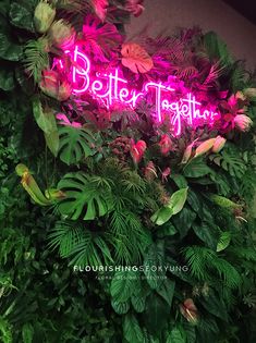 a neon sign that says better together surrounded by greenery and flowers on the wall