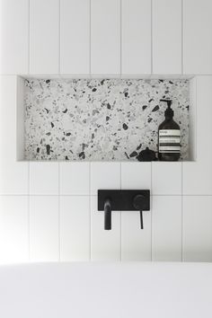 a bathroom with white tile and black faucet on the wall next to soap dispenser