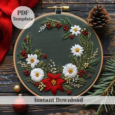 an embroidered christmas wreath with poinsettis and pine cones on a wooden table