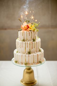 a three tiered cake with flowers and sparklers on top is sitting on a table