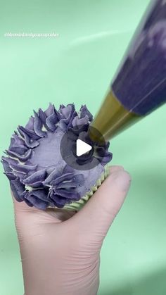 a hand holding a cupcake with purple frosting