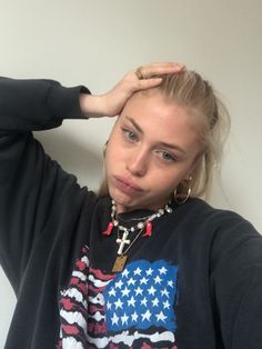 a woman with her hand on her head and wearing an american flag shirt, standing against a white wall