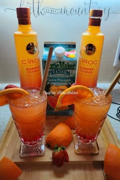 two glasses filled with orange juice and strawberries on top of a wooden table next to bottles