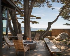 an outdoor fire pit on a deck with chairs and tables next to the water's edge