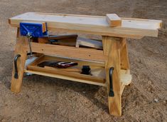 a bench made out of wood with tools on it in the sand and dirt area