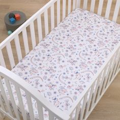 a white crib with a pink, blue and green paisley print sheet on it