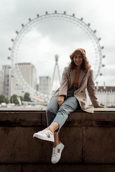 a woman sitting on top of a stone wall next to a ferris wheel in the background