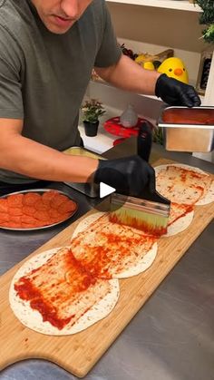 a man is making pizzas on a wooden cutting board with spatula and sauce