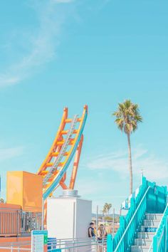 a roller coaster ride at an amusement park with palm trees in the foreground and people walking around