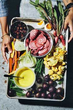 a tray filled with vegetables and sauces on top of a cement floor next to two hands