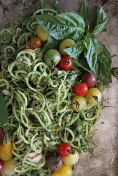 a pile of green pasta with tomatoes and spinach on the top, surrounded by basil leaves