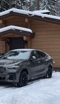 a grey bmw suv parked in front of a house with snow on the ground and trees