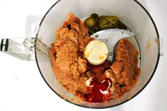 a food processor filled with meat and vegetables on top of a white counter next to an olive