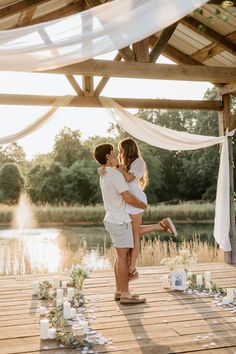 a man holding a woman in his arms as they stand on a wooden platform with flowers and candles around them