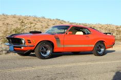 an orange muscle car is parked on the side of the road in front of a hill