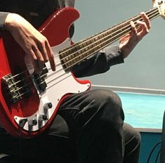 a man sitting in a chair playing a red bass guitar with his hands on it