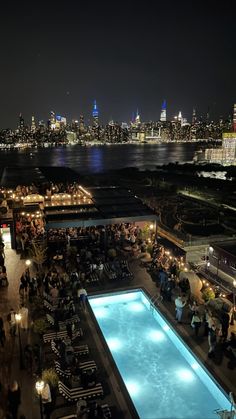 an outdoor swimming pool at night with city lights in the background and people sitting around it