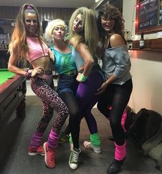 four women posing for the camera in front of a pool table at a bar with neon colored leggings