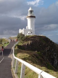 a white lighthouse on top of a hill next to the ocean with cars driving down it