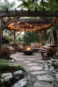 Cozy outdoor patio with string lights, surrounded by benches, chairs, plants, and a fire pit in the center. Backyard Garden Oasis Landscaping Ideas, Outdoor Home Inspiration, Small Backyard Oasis On A Budget Cozy, Backyard Country Ideas, Diy Fire Pit Patio Cheap, Farmhouse Firepits Backyard Ideas, Back Patio Entertainment Area, Fire Pit With Pergola Ideas Backyard, Outdoor Peaceful Space