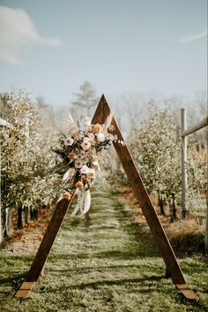 a wedding arch decorated with flowers and feathers in the middle of an apple tree orchard