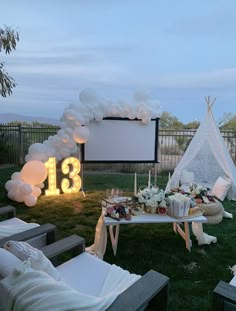 an outdoor movie party setup with balloons, candles and decorations on the grass near a teepee tent