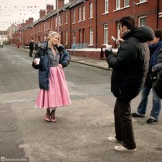 a woman in a pink skirt is standing on the street while a man takes a photo