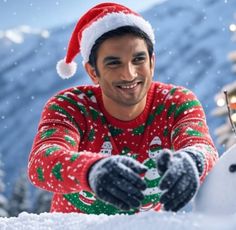 a man in a christmas sweater and santa hat making a snowman out of the snow