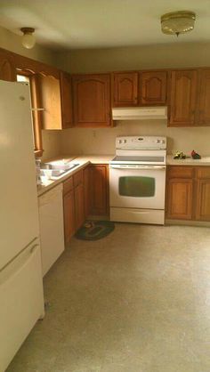 an empty kitchen with white appliances and wood cabinets in the middle of the flooring