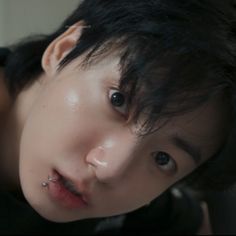 a close up of a person with black hair and piercings on his nose looking at the camera