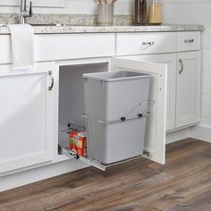 a kitchen with white cabinets and wooden floors has a pull out trash can in the corner