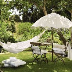 there is a hammock set up in the yard with two chairs and an umbrella