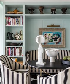 two chairs and a table in front of bookshelves with vases on them