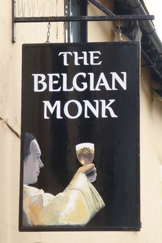 a black sign hanging from the side of a building that reads, the belgan monk