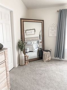 a large mirror sitting on top of a wooden dresser next to a white bed in a bedroom