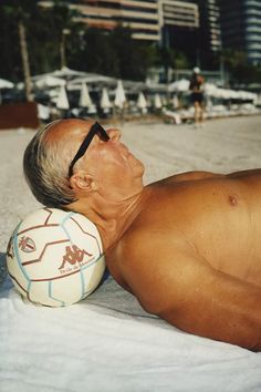 an older man laying on the beach with a soccer ball