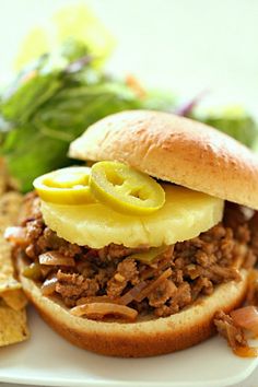 a pulled pork sandwich on a plate with potato chips and lettuce next to it