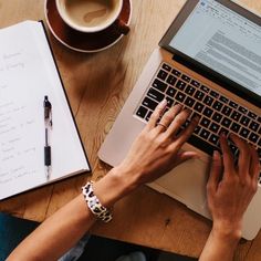 a person using a laptop computer on top of a wooden table next to a cup of coffee