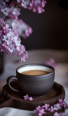 a cup of coffee sitting on top of a saucer filled with liquid next to purple flowers