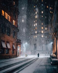 a city street at night with snow falling on the ground and people walking down the sidewalk