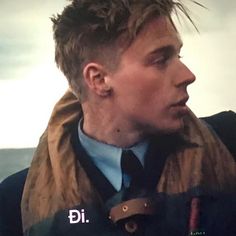 a man wearing a jacket and tie standing in front of the ocean looking off into the distance