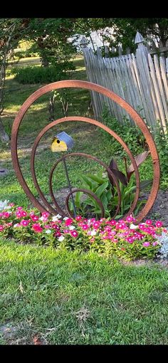 a bird sitting on top of a metal sculpture in the grass next to pink flowers