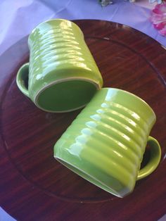 two green cups sitting on top of a wooden plate