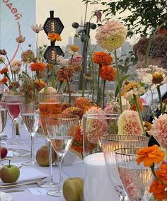 there are many wine glasses on the table with flowers and fruit in them, all lined up