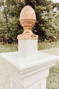 an ornate gold and white urn on top of a pillar in front of some trees