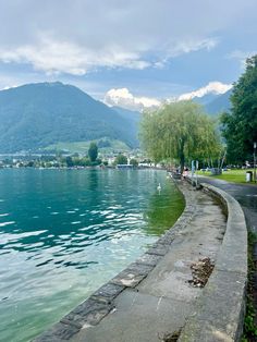 people are walking along the edge of a body of water with mountains in the background