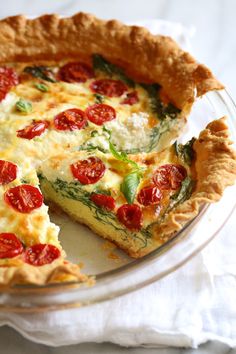 a quiche with tomatoes and spinach is on a glass plate, ready to be eaten